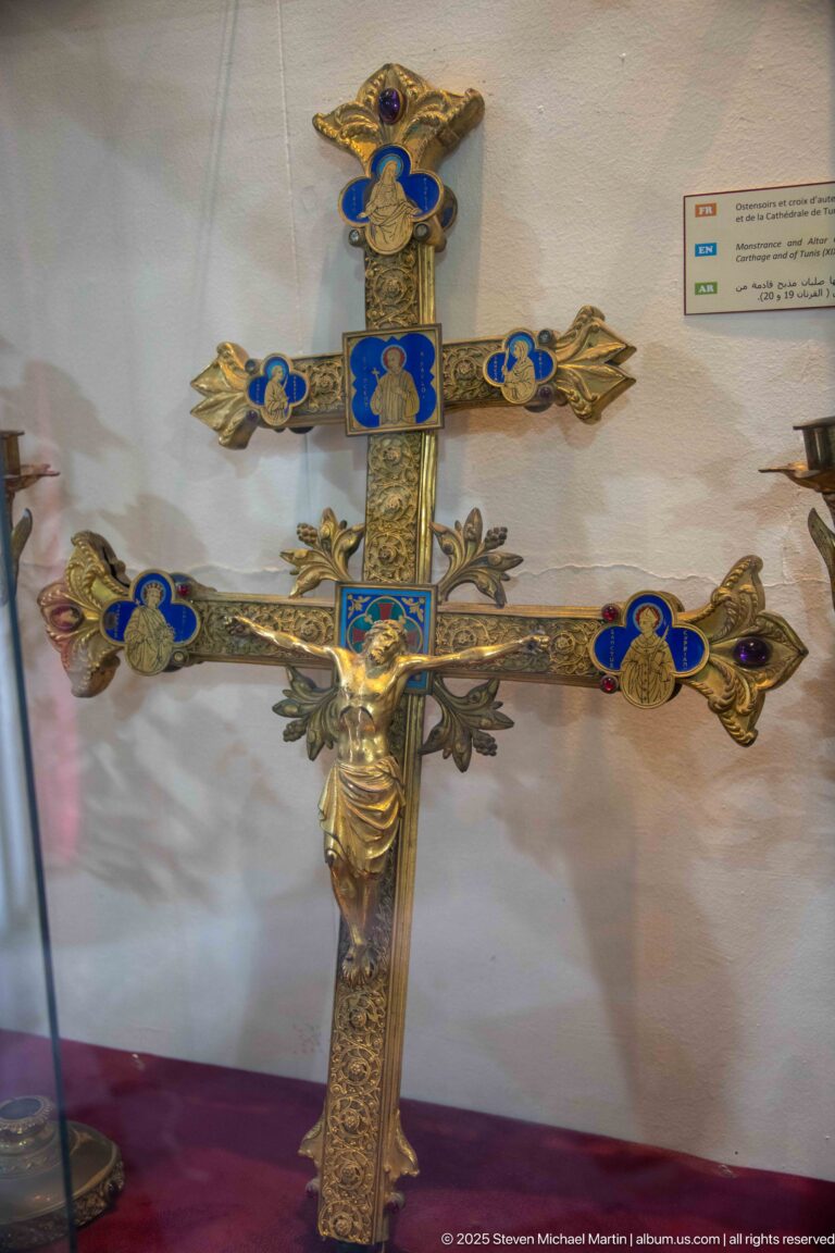 Gilded double-barred devotional cross with blue enamel medallions, foliate terminals, and a small sculpted figure of Christ.