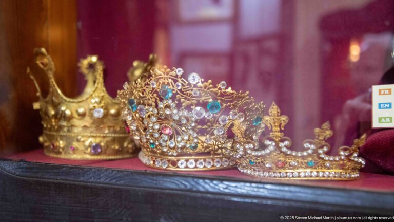 Several jeweled devotional crowns in a glass case, including an openwork crown densely set with colored stones and pearls.