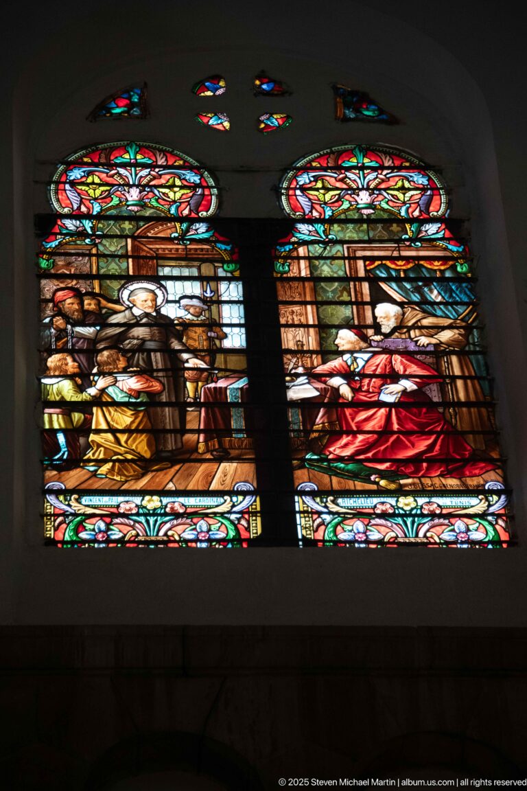 Two adjacent stained-glass narrative panels with grouped figures beneath matching floral headers and small colored openings above.