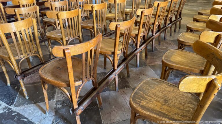 Rows of worn wooden cathedral chairs arranged in close blocks beside narrow dividing rails and aisles.