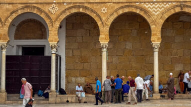 People standing, walking, and sitting beneath pointed courtyard arches and slender columns at the Zitouna Grand Mosque.
