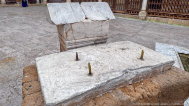 Weathered pale stone slab with several short metal pegs beside a heavier carved stone block in the mosque courtyard.
