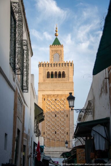 Upper stage of the Zitouna Grand Mosque minaret with geometric panel, arched openings, crenellations, and green-tiled cap.