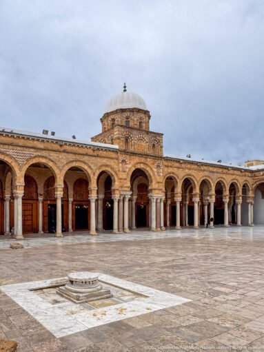 Wide Zitouna Grand Mosque courtyard with arcades, slender columns, and a domed central bay rising above the prayer hall.
