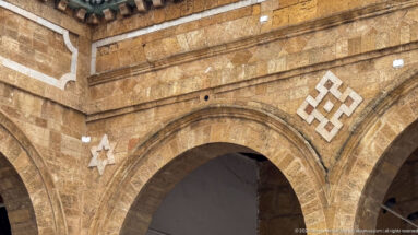 Warm stone courtyard arch decorated with white geometric inlays, including an eight-pointed star and interlaced knot.