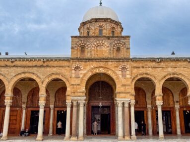 Frontal view of the Zitouna Grand Mosque prayer-hall façade with central arched entrance, ribbed dome, and flanking arcades.
