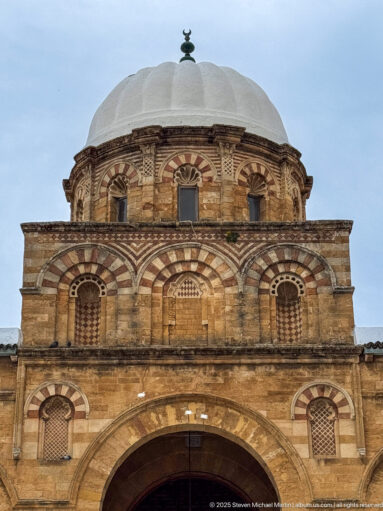 Close view of the Zitouna Grand Mosque central domed bay with striped arches, grilled openings, and a pale ribbed dome.