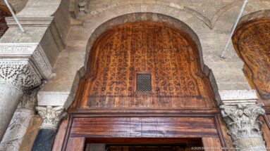 Large arched carved wooden screen with a small central grille, framed by stone columns and ornate capitals.