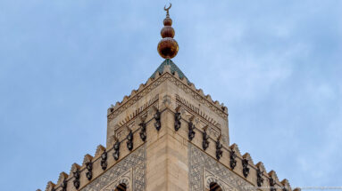 Upper stage of the Zitouna Grand Mosque minaret with patterned stonework, crenellations, pyramidal cap, stacked finial, and crescent.