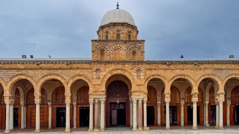 Frontal Zitouna Grand Mosque prayer-hall façade with central dome, tall entrance arch, and symmetrical flanking arcades.