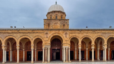 Frontal Zitouna Grand Mosque prayer-hall façade with central dome, tall entrance arch, and symmetrical flanking arcades.
