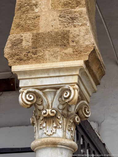 Close-up of a pale carved stone capital with large volutes and leaf ornament beneath a warm masonry block.