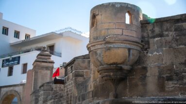 Rounded projecting stone turret with narrow opening and corbelled base on a dark fortified wall.
