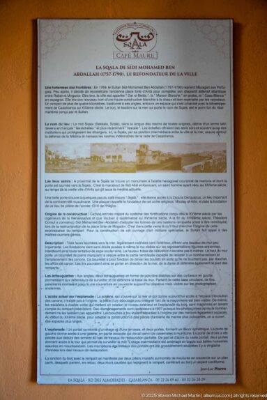 French-language information panel mounted on an ochre wall, with a small site plan and dense explanatory text.