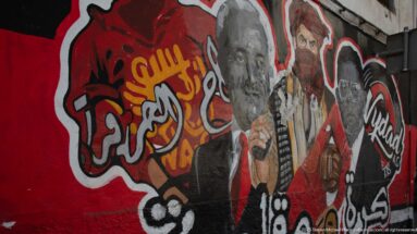 Large red, black, and white street mural with several painted portraits and graffiti-style lettering.