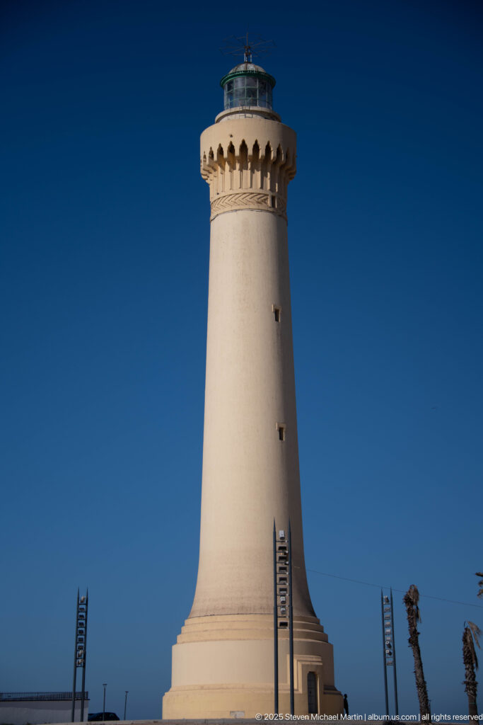 White tapered lighthouse tower with projecting lantern gallery rising against a deep blue sky.