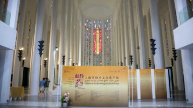 Long white nave of the former Sacred Heart Church leading to tall multicolored stained-glass windows and an exhibition display.