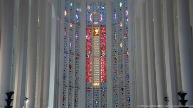 Large multicolored stained-glass window framed by tall white structural ribs inside the former Sacred Heart Church.