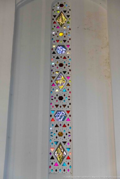 Narrow vertical stained-glass panel with repeated diamond shapes in red, blue, yellow, green, and clear glass.