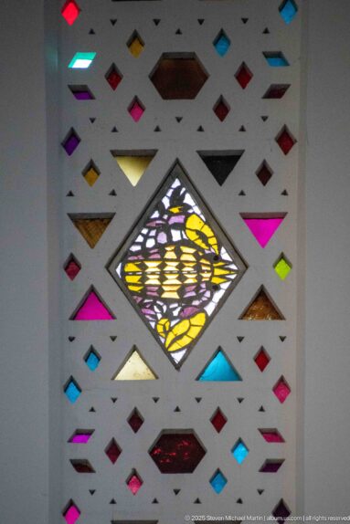 Floral stained-glass medallion in a diamond frame surrounded by small brightly colored geometric panes.
