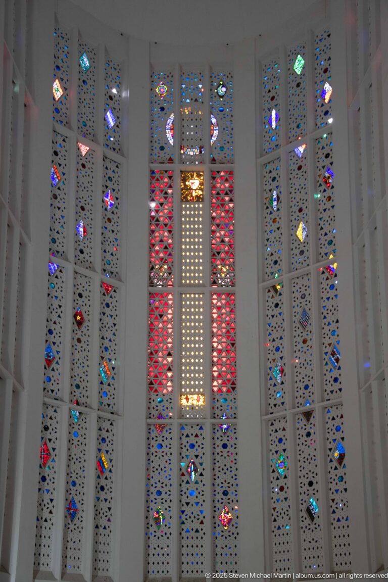 Central red-and-white stained-glass panels flanked by narrow multicolored geometric windows inside the former church.