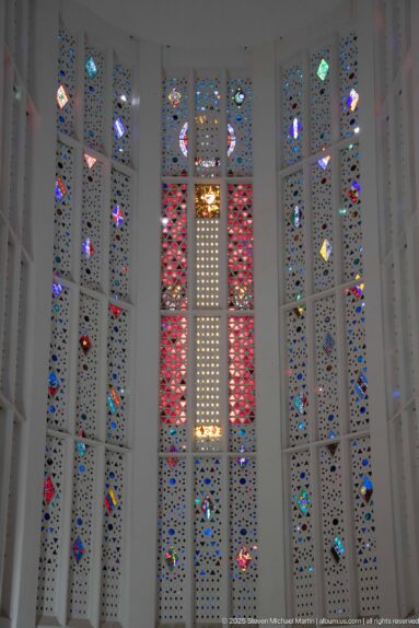 Central red-and-white stained-glass panels flanked by narrow multicolored geometric windows inside the former church.