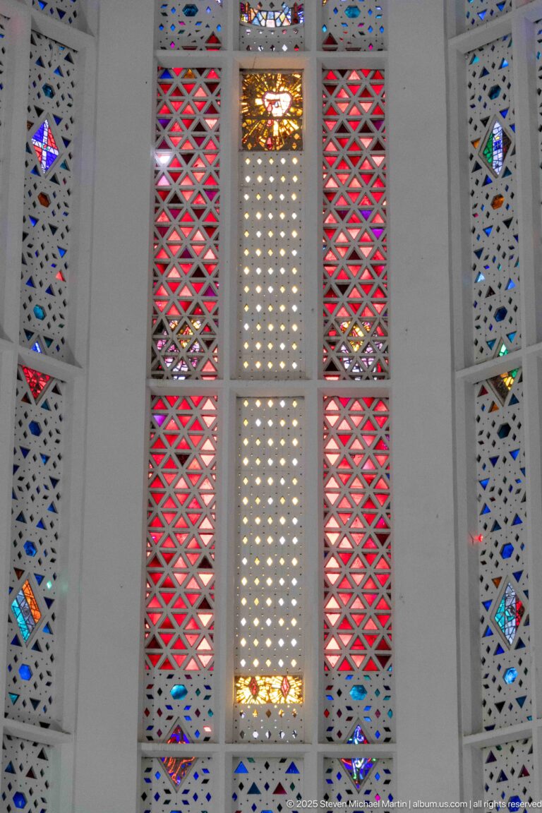 Close view of red triangular stained-glass lattice flanking a pale perforated central panel with small colored accents.