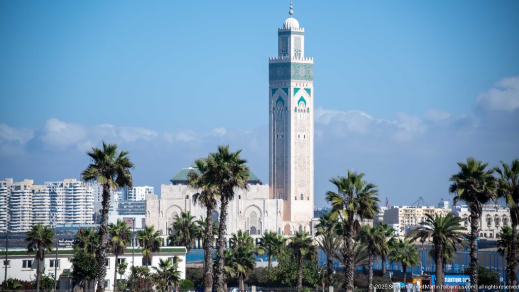 Hassan II Mosque minaret rising above palms and the mosque complex, with Casablanca apartment blocks in the background.