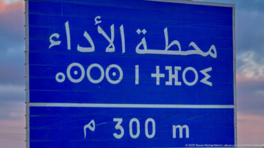 Blue Arabic road sign with white lettering and symbols indicating a facility 300 meters ahead.