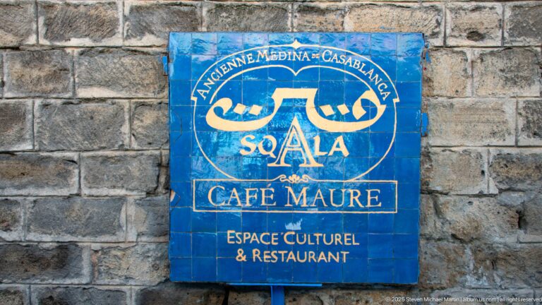 Blue tiled Sqala Café Maure sign with Arabic and French lettering mounted on a rough stone wall.