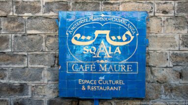 Blue tiled Sqala Café Maure sign with Arabic and French lettering mounted on a rough stone wall.