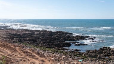 Wide Atlantic view over a dark wave-cut rock platform with shallow channels, breaking surf, and open horizon.