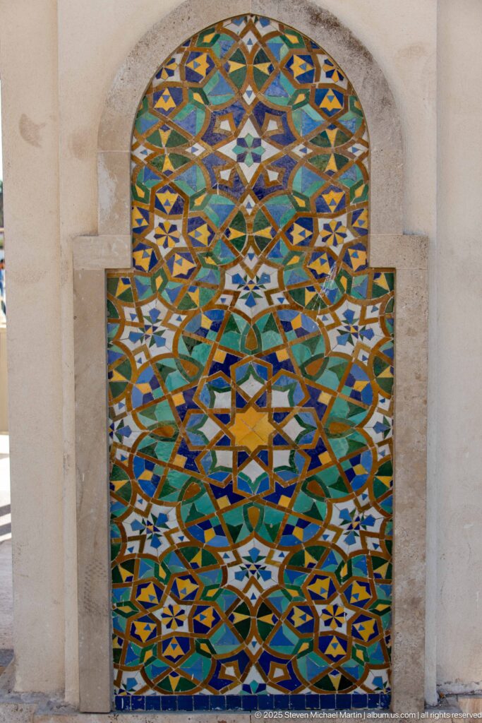 Arched multicolored zellij panel with layered stars and interlaced geometric bands in a pale stone recess.