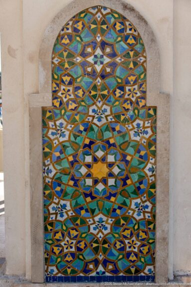 Arched multicolored zellij panel with layered stars and interlaced geometric bands in a pale stone recess.