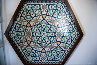 Hexagonal framed mosaic with multicolored interlaced star geometry and a central radial motif.