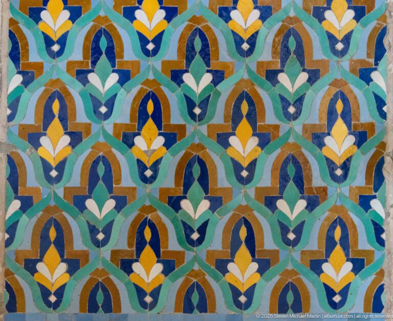 Repeating stylized floral mosaic in turquoise, blue, green, white, ochre, and yellow.