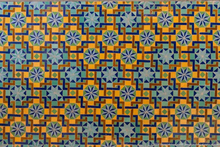 Close-up of repeating pale blue stars within orange, turquoise, green, and dark blue geometric zellij.