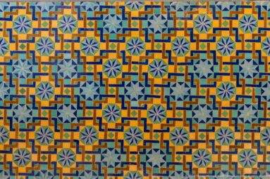 Close-up of repeating pale blue stars within orange, turquoise, green, and dark blue geometric zellij.