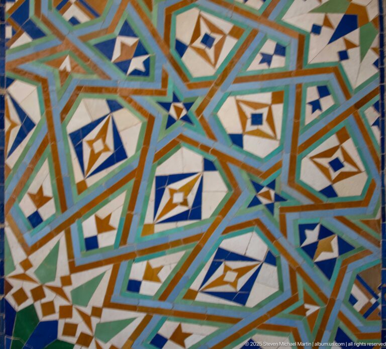 Close view of angular turquoise, green, white, blue, and ochre geometric mosaic.