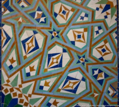 Close view of angular turquoise, green, white, blue, and ochre geometric mosaic.