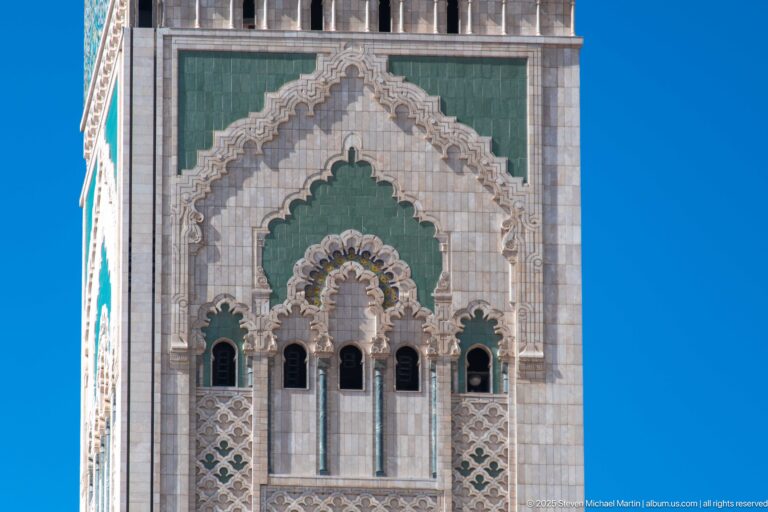 Close view of Hassan II Mosque minaret with green panels, carved arches, windows, and geometric ornament.