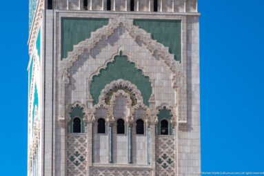 Close view of Hassan II Mosque minaret with green panels, carved arches, windows, and geometric ornament.