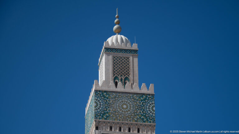 Upper Hassan II Mosque minaret with geometric mosaic panel, white crown, and stacked spherical finials.