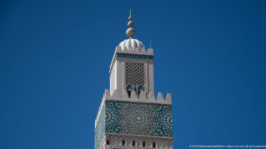 Upper Hassan II Mosque minaret with geometric mosaic panel, white crown, and stacked spherical finials.