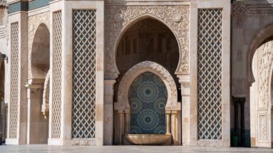 Blue-green wall fountain beneath a carved horseshoe arch, flanked by tall patterned screens.