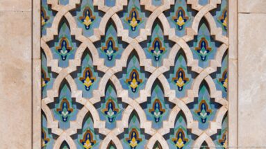 Close view of repeating pointed interlaced mosaic forms in turquoise, blue, green, yellow, and white.