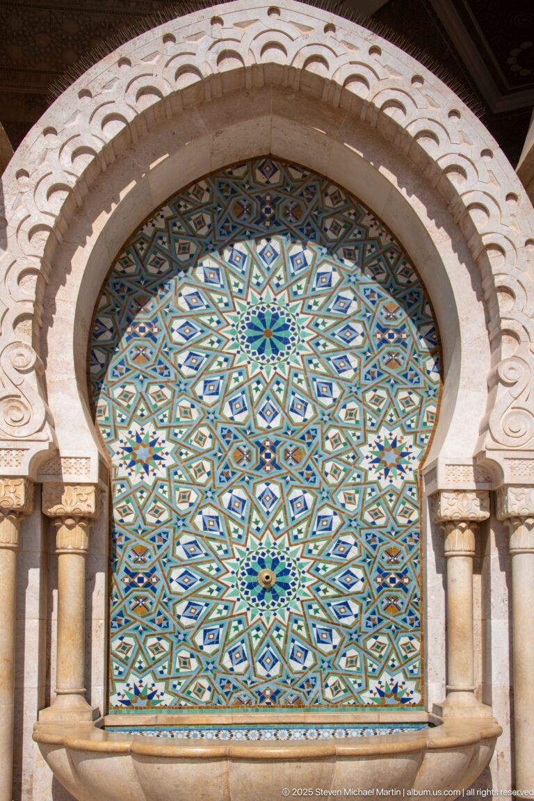Arched exterior panel filled with blue-green geometric mosaic and framed by small columns.