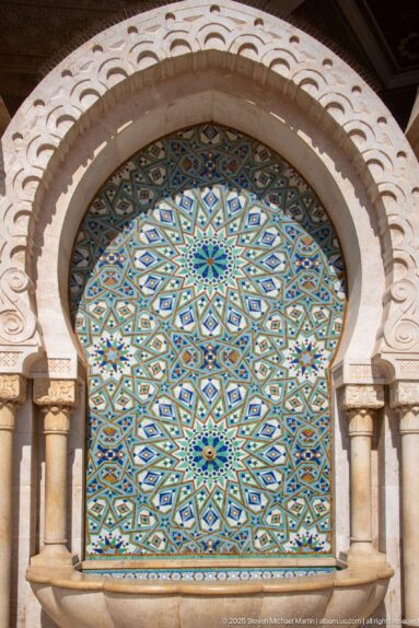 Arched exterior panel filled with blue-green geometric mosaic and framed by small columns.
