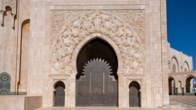 Monumental pointed portal with carved pale surround, metal door, and smaller side openings.