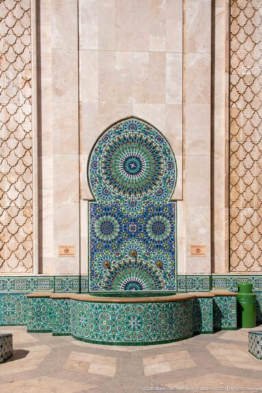 Broad low fountain beneath an arched blue-green mosaic panel on a pale stone wall.